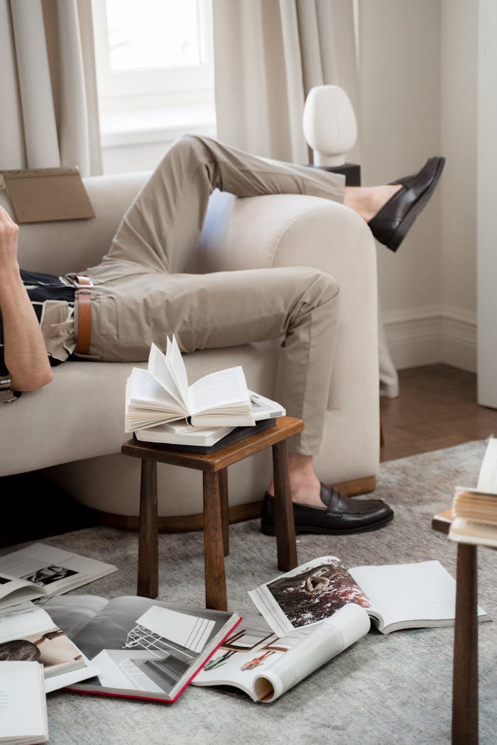 about-img Man reclines on a sofa surrounded by open books in a cozy living room, conveying relaxation and leisure.