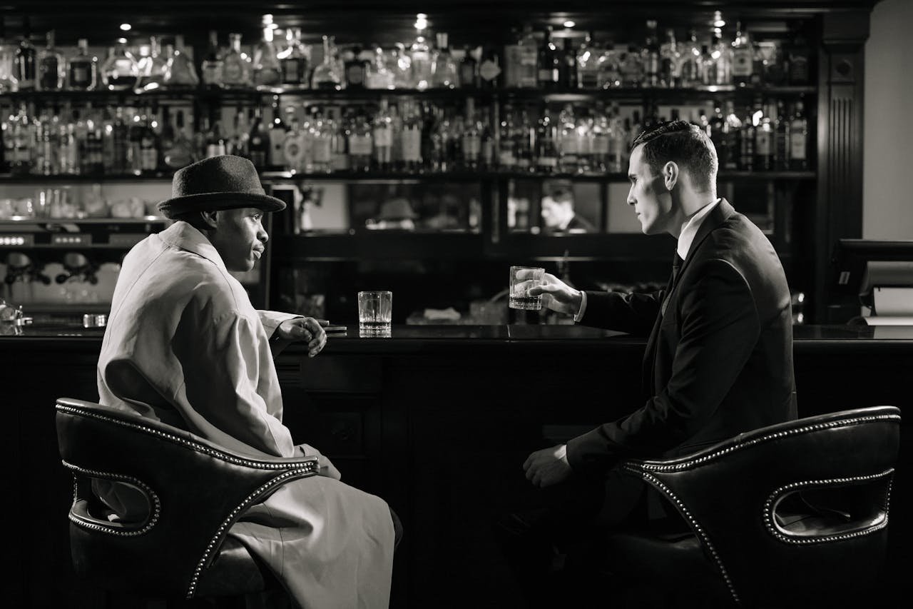 hero-img-01 A cinematic, noir-style meeting in a dimly lit bar with a tense atmosphere.