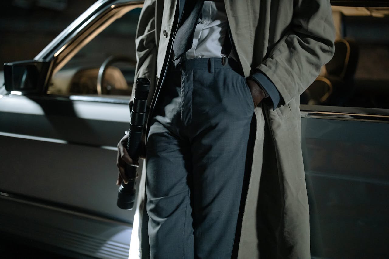 our-services-3 Close-up of a person in a trench coat holding a flashlight near a car at night.